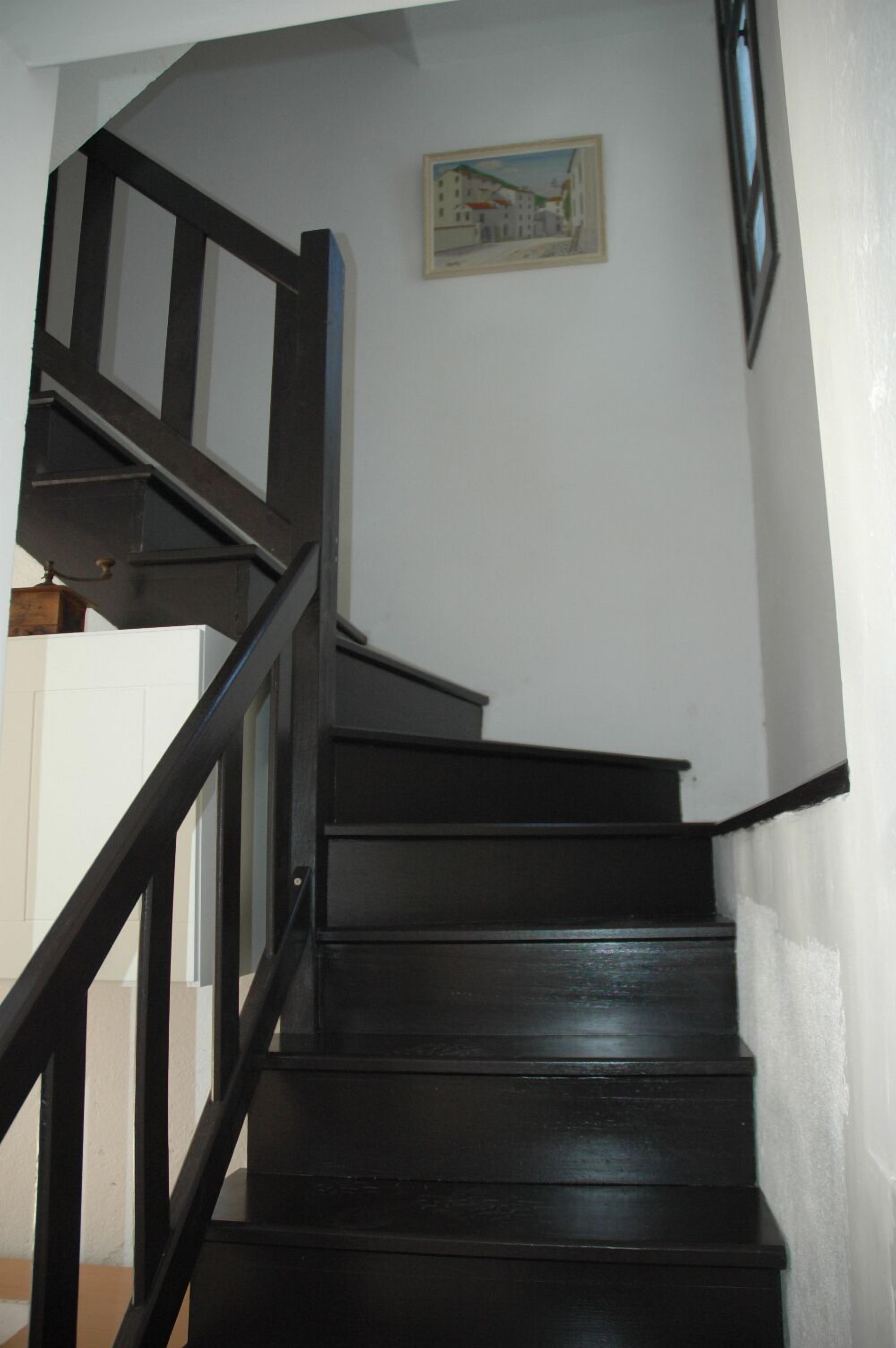 Eine schwarze Holztreppe mit Handlauf, die zu einer oberen Etage führt.
