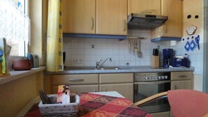 A compact kitchen with wooden cabinets, a built-in oven, and a sink. There's a table with a patterned tablecloth and a basket with items on it.