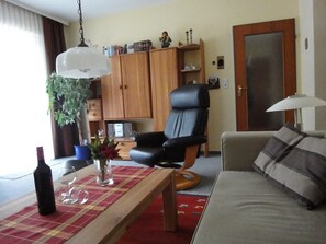 A living room with a sofa, a coffee table, a black chair, a wooden cabinet, and a hanging light fixture. - 4-star apartment near the center - bicycles free of charge (Bad Zwischenahn)