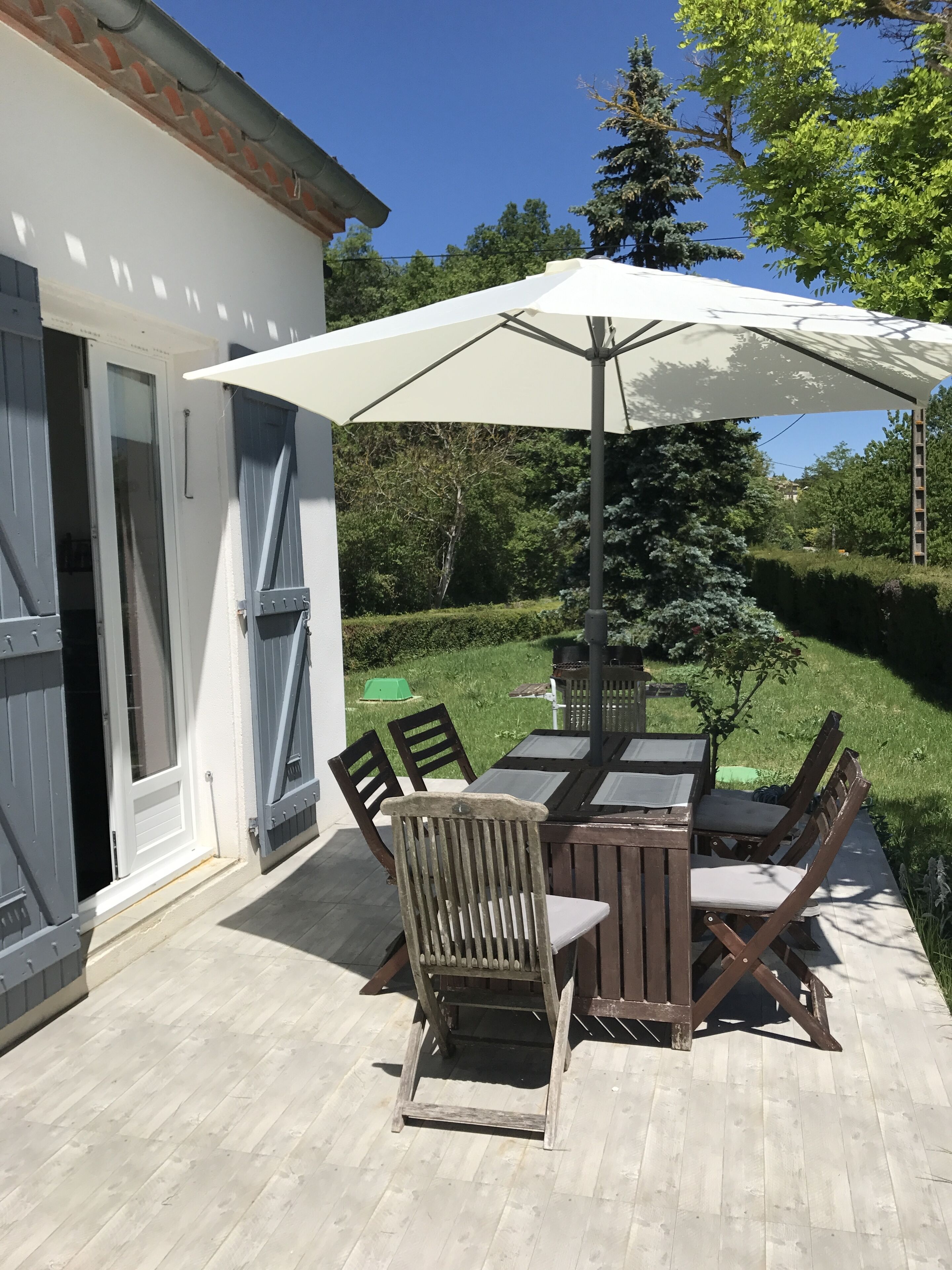 Un patio con un edificio blanco, una mesa de madera y sillas.