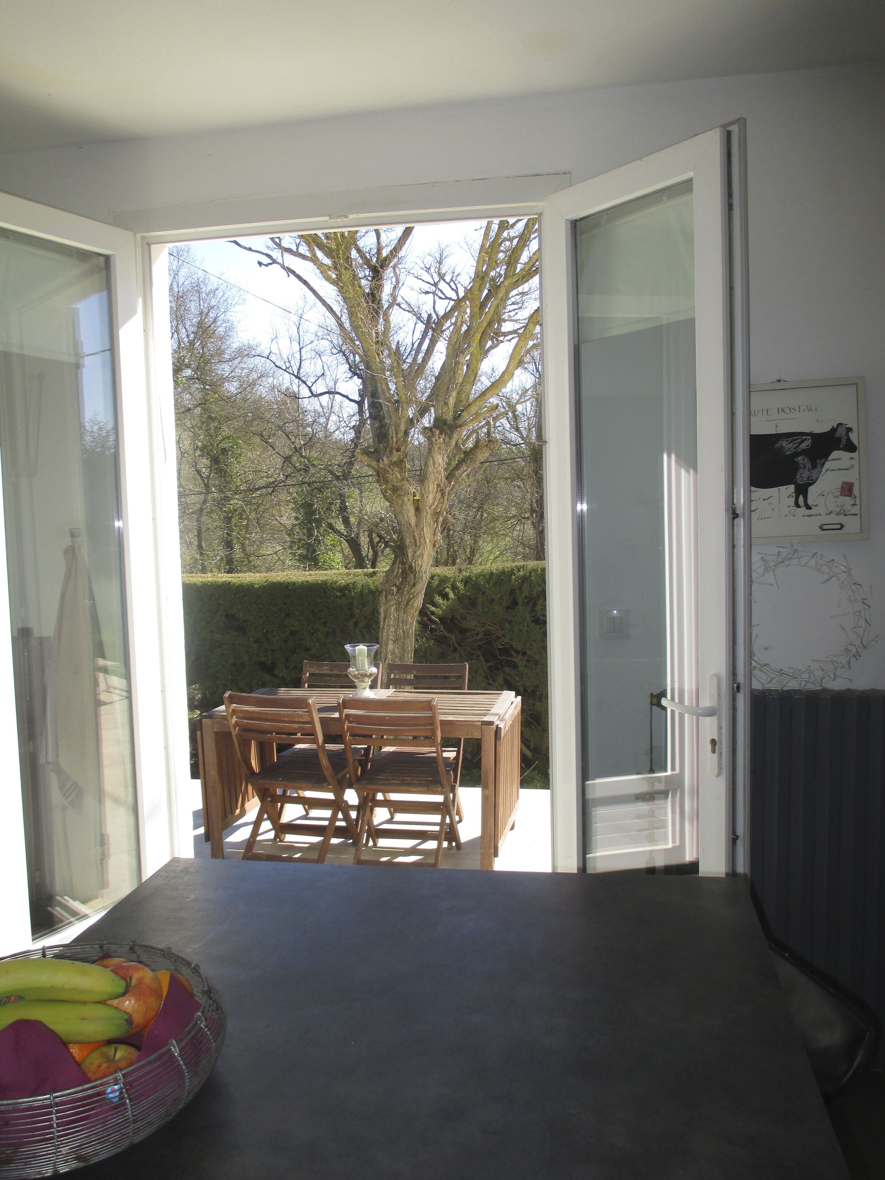 An open door leading to a dining area with a table and chairs, a fruit bowl on the table, and a framed picture on the wall.