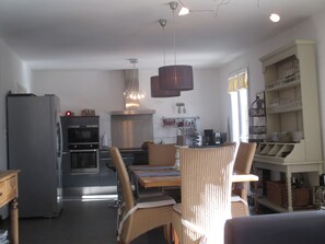 A modern kitchen with a built-in oven, a dining area with wicker chairs, and a coffee station.