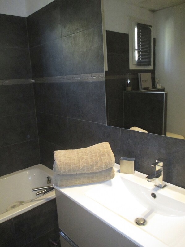 A modern bathroom with dark tiles, a white sink, and a bathtub.