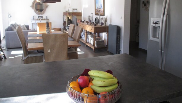 Una cocina moderna con un frutero en la encimera, un rincón de comedor con sofá y sillas, y un refrigerador.