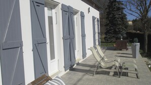 Un edificio con grandes puertas correderas, un espacio al aire libre cubierto con sillas y cojines, y una vista de árboles y un edificio lejano.