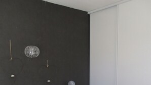 Un dormitorio con cama, almohadas, una mesita de noche con lámpara, y una lámpara de pared.