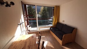 A room with a wooden table, a sofa, a sliding glass door leading to a balcony, and a view of trees. - Arc 1800 - Studio with balcony overlooking Montblanc, at the foot of the slopes for 5 people. (Bourg-Saint-Maurice)