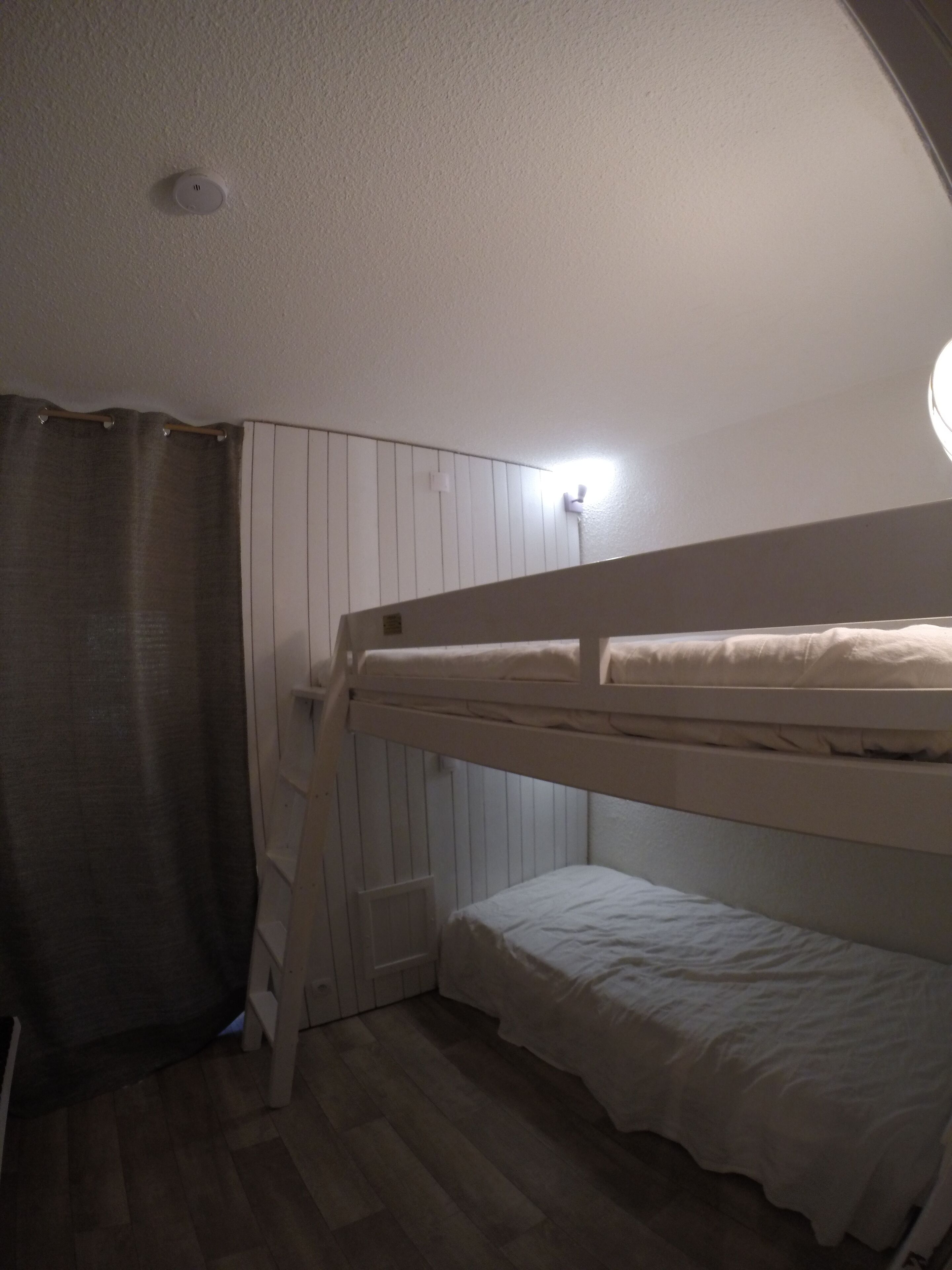 Une chambre avec un lit superposé, un rideau, un luminaire et un radiateur.