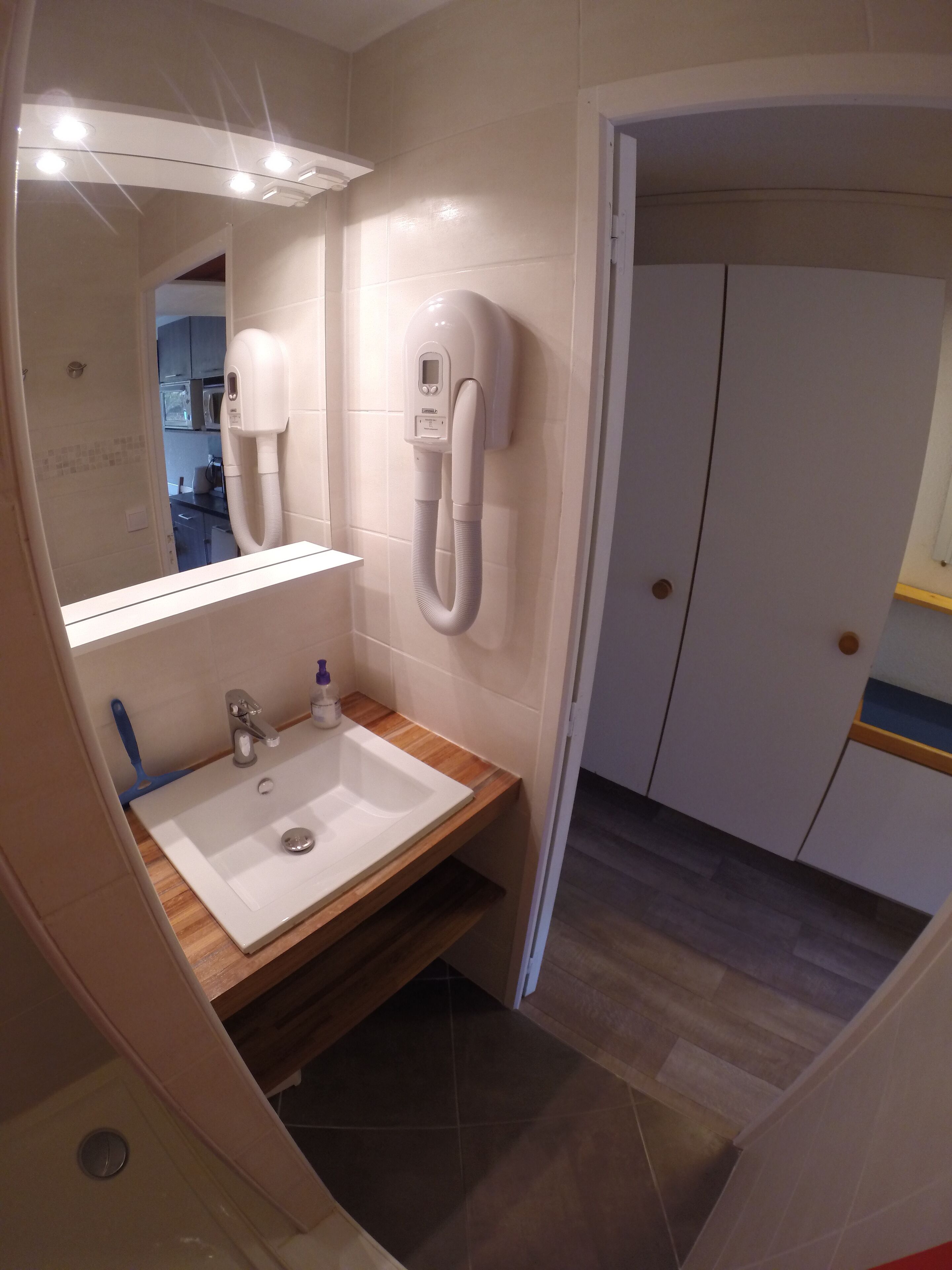 Un baño con lavamanos blanco, un espejo y un secador de pelo montado en la pared.