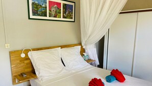 Cama bem arrumada com lençóis brancos, cabeceira de madeira, mesa de cabeceira com abajur e quadro na parede.
