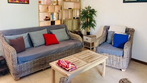 Uma sala de estar com sofá, uma poltrona, mesa de centro, estante de livros e um vaso de planta.