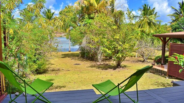 Um terraço com duas cadeiras verdes, com vista para um jardim e o mar.