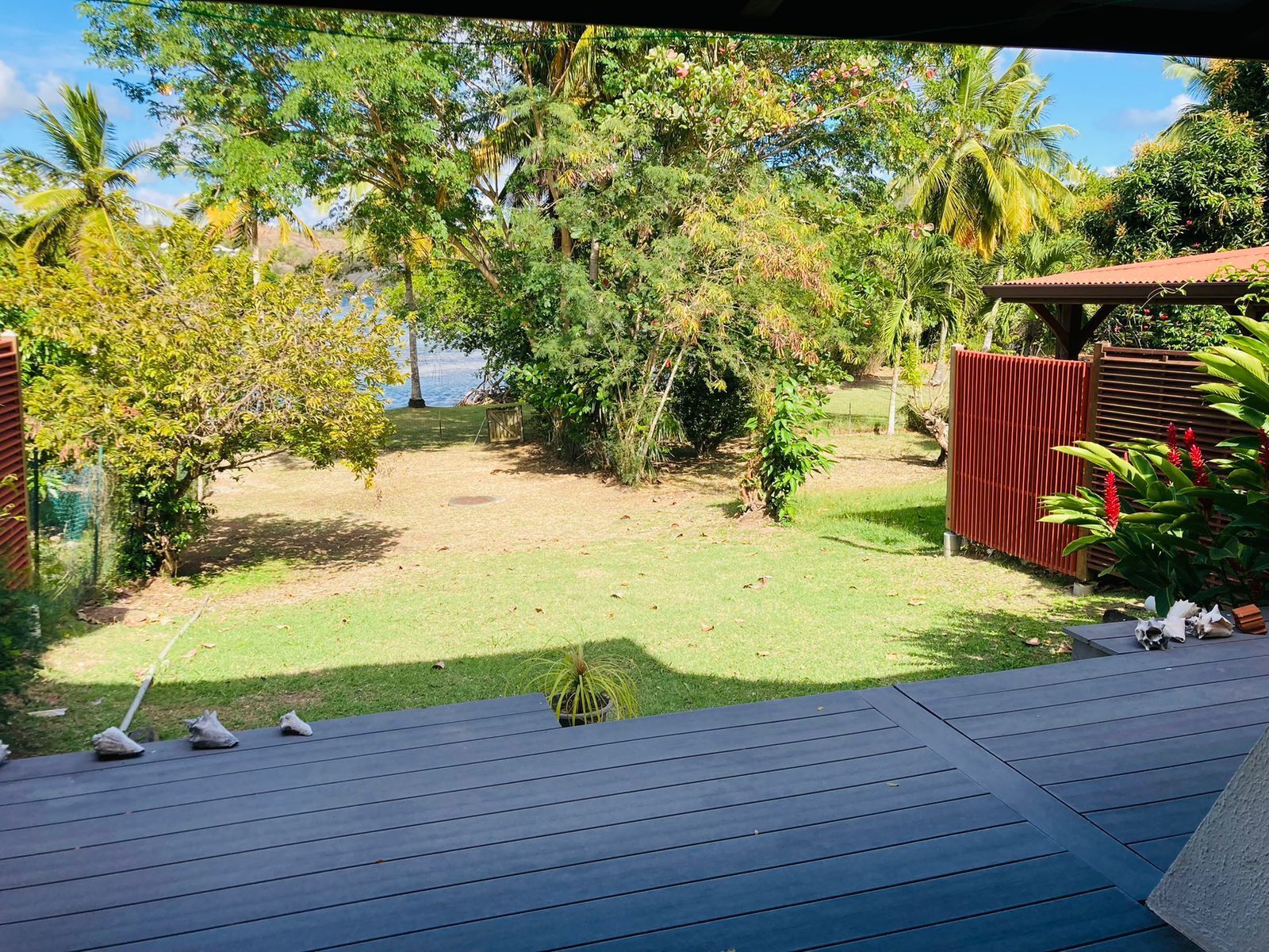 Vista de un patio trasero con terraza de madera, una pequeña zona de jardín y un cerramiento.