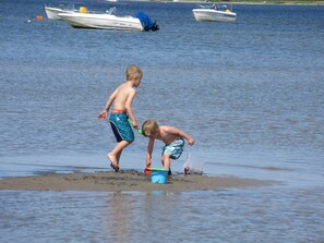 Zwei Kinder spielen in der Nähe von Wasser, im Hintergrund sind Boote zu sehen.