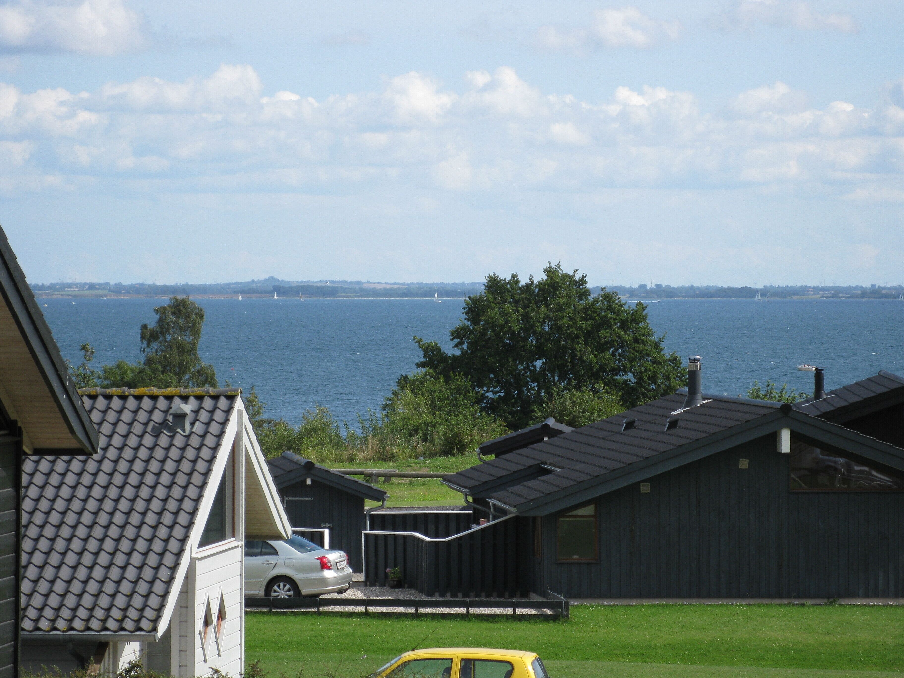 A residential area with a view of a large body of water, a car parked in the driveway, and a building with a dark roof and windows.