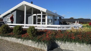 Et moderne hus med stor veranda, et overdækket udendørsareal og en velplejet have med røde blomster.