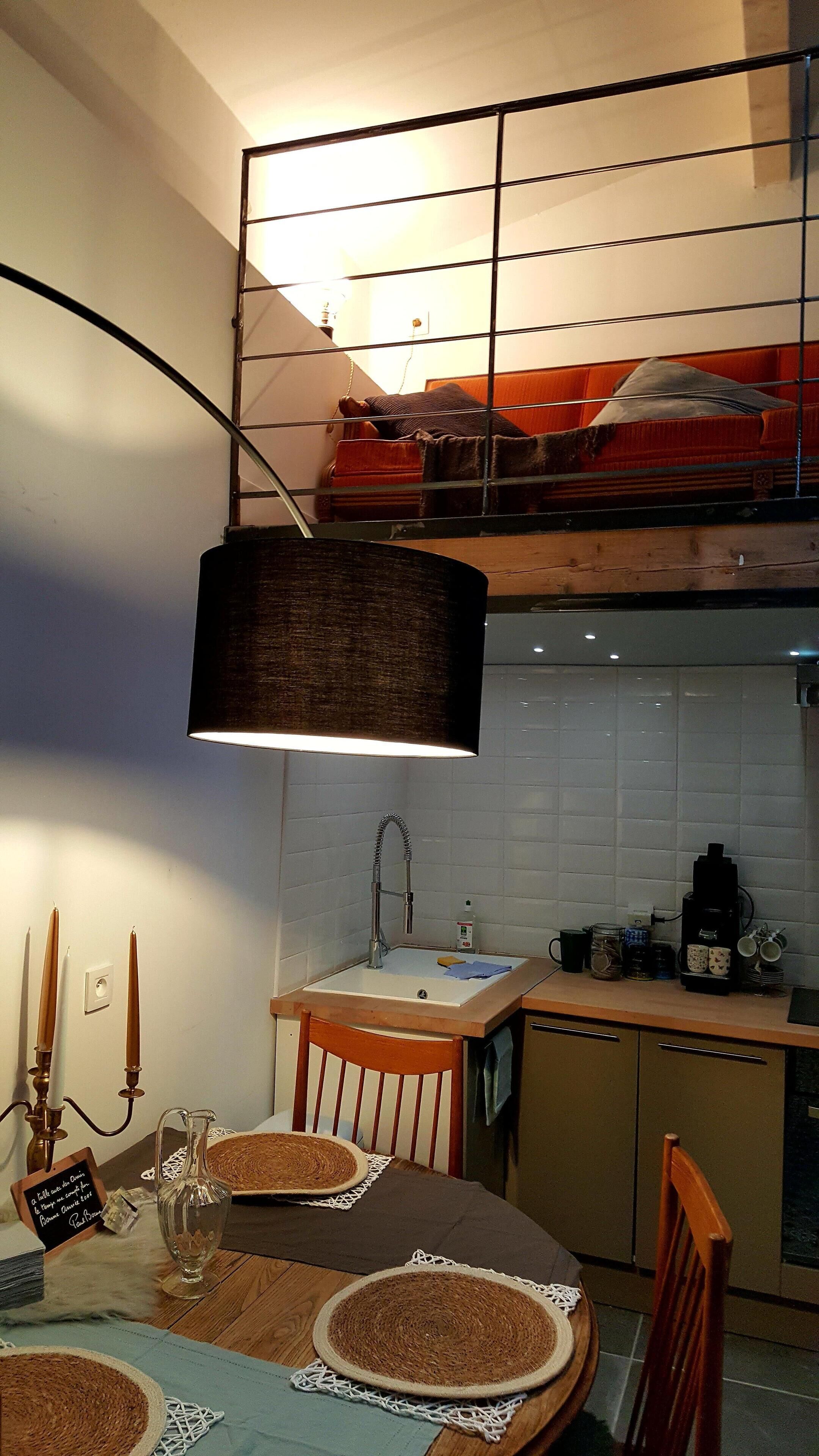 Une cuisine compacte avec une table en bois, un luminaire suspendu et une étagère intégrée au-dessus du plan de travail.