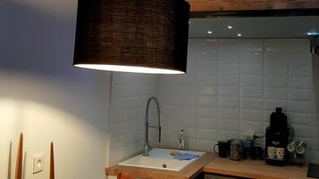 Une cuisine compacte avec une table en bois, un luminaire suspendu et une étagère intégrée au-dessus du plan de travail.
