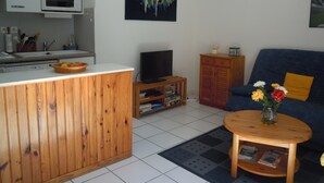 A compact living space with a kitchenette, a television, a sofa, and a small coffee table with a vase of flowers.