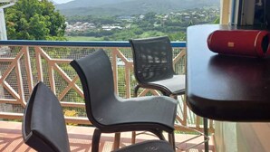 A balcony with two black chairs and a red cylindrical object, overlooking a scenic landscape with mountains and greenery. - Villa with private saltwater pool and panoramic view of the sea and Diamond Rock. (RIVIERE SALEE)