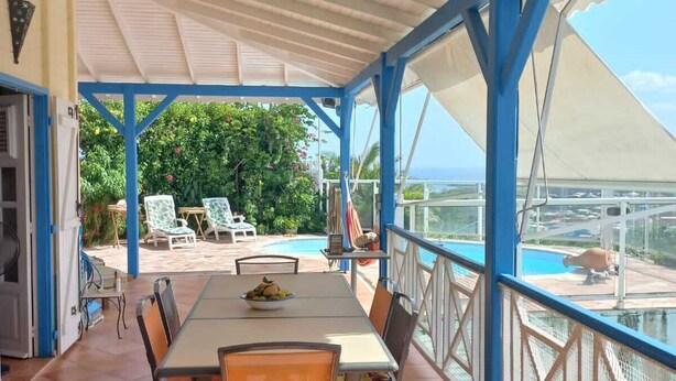 A covered outdoor dining area with a table and chairs, a pool in the background, and a view of the ocean. - Villa with private saltwater pool and panoramic view of the sea and Diamond Rock. (RIVIERE SALEE)
