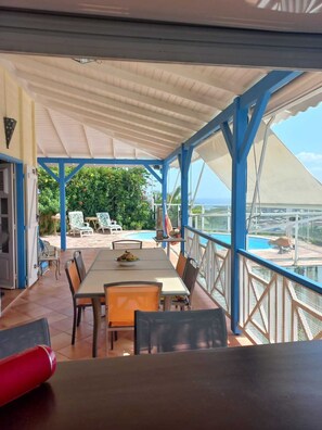 A covered outdoor dining area with a table and chairs, a pool in the background, and a view of the ocean. - Villa with private saltwater pool and panoramic view of the sea and Diamond Rock. (RIVIERE SALEE)