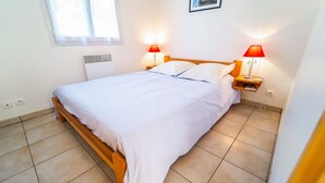Una cama bien hecha con sábanas blancas, cabecera de madera y dos lámparas de noche con pantallas rojas.