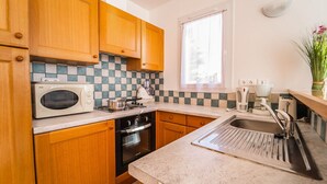 Una cocina compacta con armarios de madera, un microondas, una estufa, un lavavajillas y un fregadero.