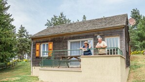 Una casa de madera rústica con balcón, antena parabólica y un pequeño jardín.