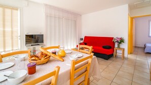 Un comedor con una mesa dispuesta para el desayuno, un sofá rojo y un televisor al fondo.