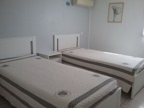Two single beds with headboards, a bedside table, a wall-mounted air conditioner, and a framed picture on the wall. - Apt. in the heart of the Alpilles, at the gates of the Camargue (Paradou)