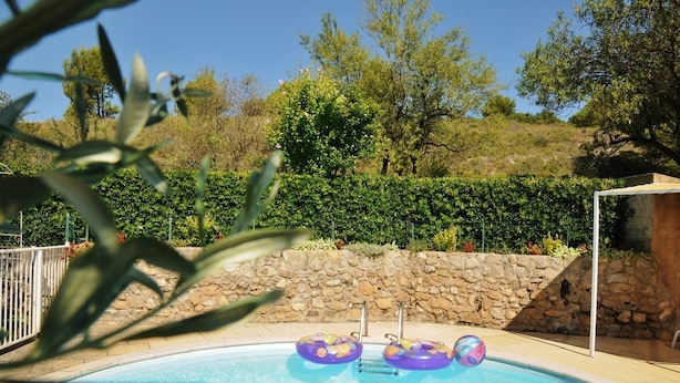 Une piscine avec trois bouées gonflables, entourée d’un mur de pierre et de verdure.