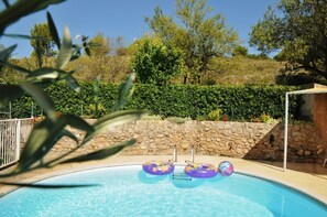 Piscina com três boias infláveis, rodeada por um muro de pedra e vegetação.
