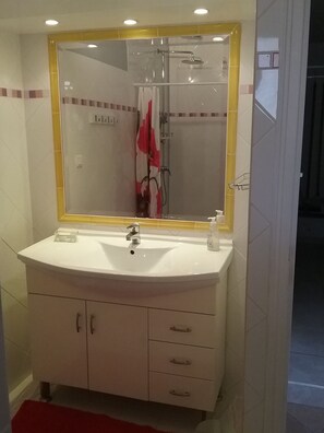 A bathroom with a white sink, a mirror with a yellow frame, and a shower area. - Apt. in the heart of the Alpilles, at the gates of the Camargue (Paradou)