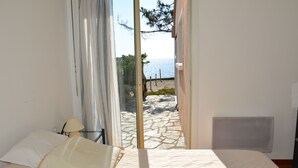 A bedroom with a bed, a lamp, and a view of the sea through a glass door.