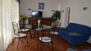 A dining area with a round table, four chairs, a television, and a blue sofa.