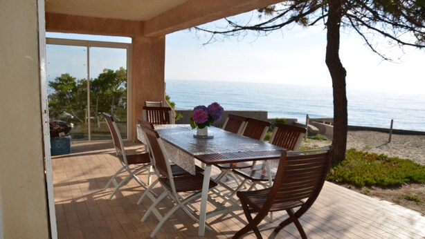 An outdoor dining area with a table and chairs, a vase with flowers, and a view of the sea.