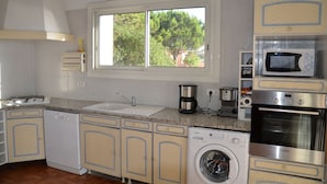 A kitchen with a washing machine, microwave, oven, and a window with a view of trees.