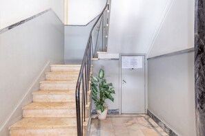Un escalier avec des marches en marbre et une rampe en métal, menant à une porte sur laquelle est apposée une plaque.