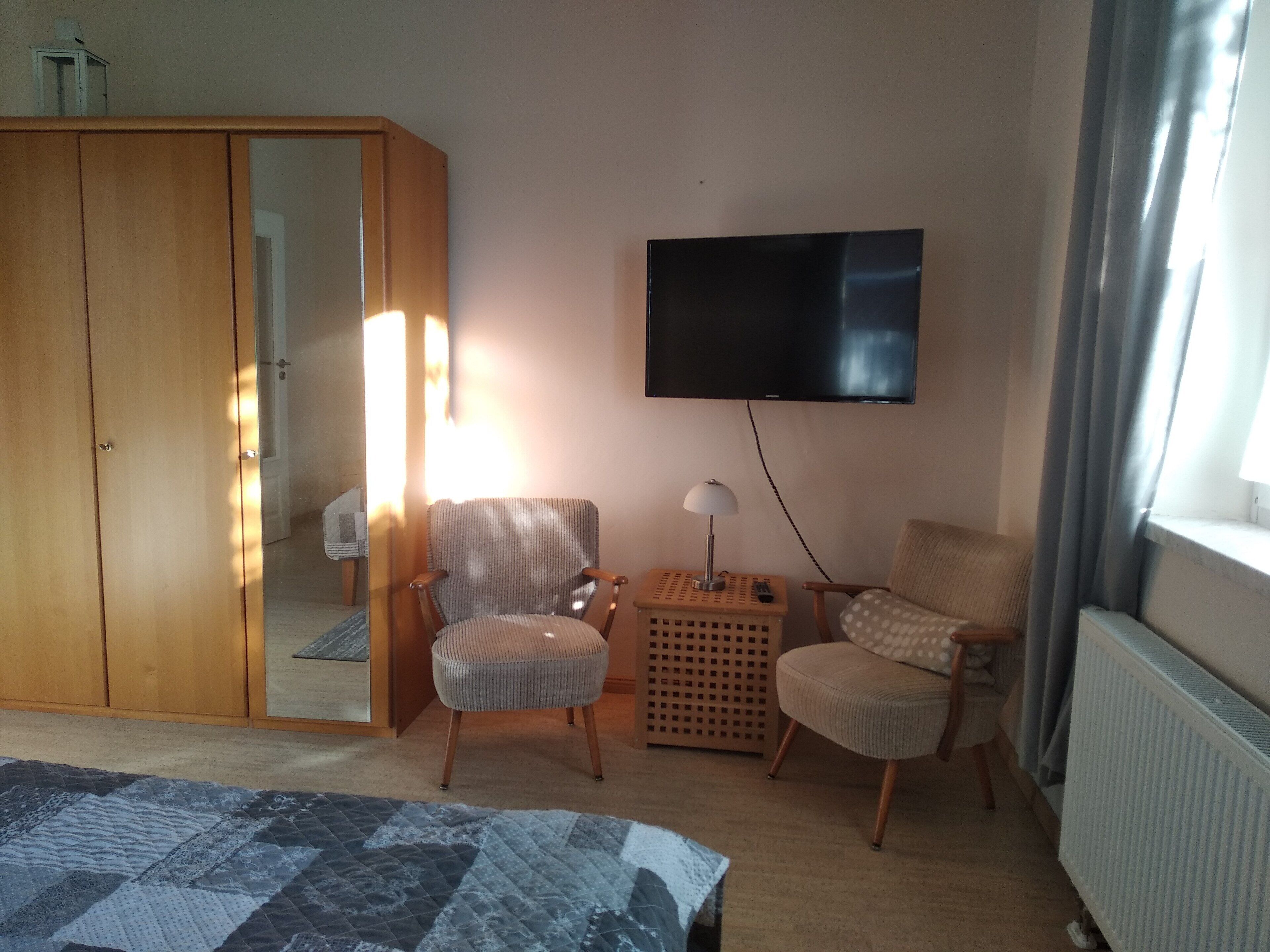A bedroom with a bed, two chairs, a TV, a wardrobe, and a radiator.