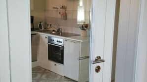A white door leading to a kitchen with a stove, oven, and a small refrigerator. - New apartment in the middle of the lake district ideal for active recreation (Blankensee)