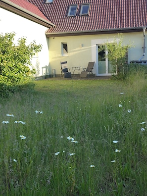 Een huis met een rood pannendak, een kleine tuin met witte bloemen en tuinmeubilair.