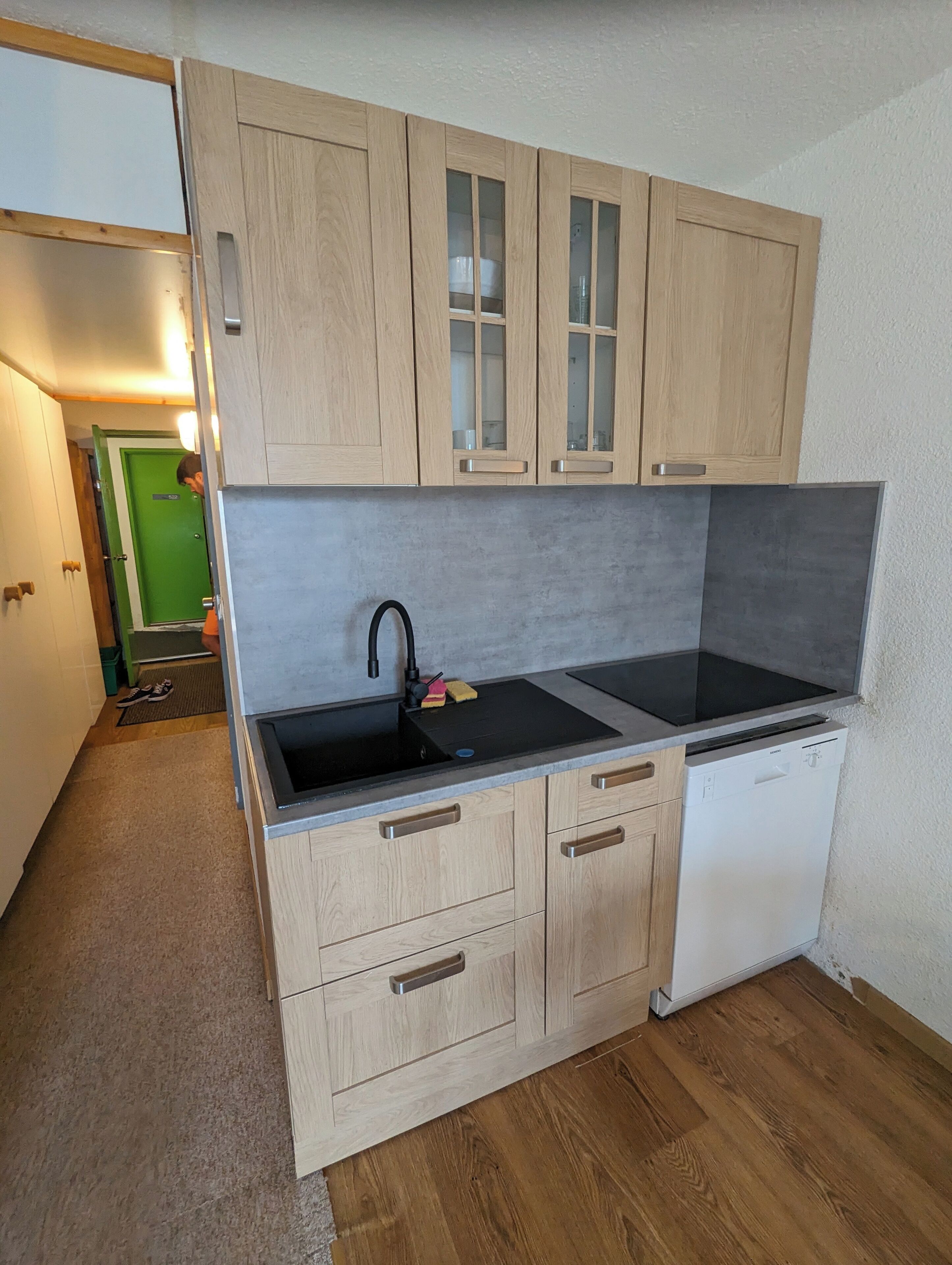 A compact kitchen with wooden cabinets, a black sink, and a built-in dishwasher.