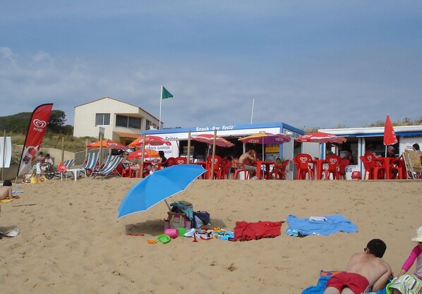 Una playa con sillas y sombrillas rojas, un bar de aperitivos y un edificio con un letrero.
