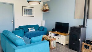 A living room with a blue sofa, a television, a wooden cabinet, and a black wood stove.