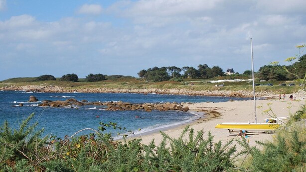 A beach with a rocky shoreline, a yellow boat, and a grassy hill with trees in the background.