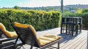 Une terrasse en bois avec deux chaises longues et une petite table, entourée de verdure et offrant une vue sur les collines.
