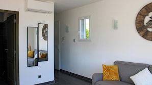 Un salon moderne avec un canapé gris, une grande horloge murale et une fenêtre donnant sur un paysage verdoyant.