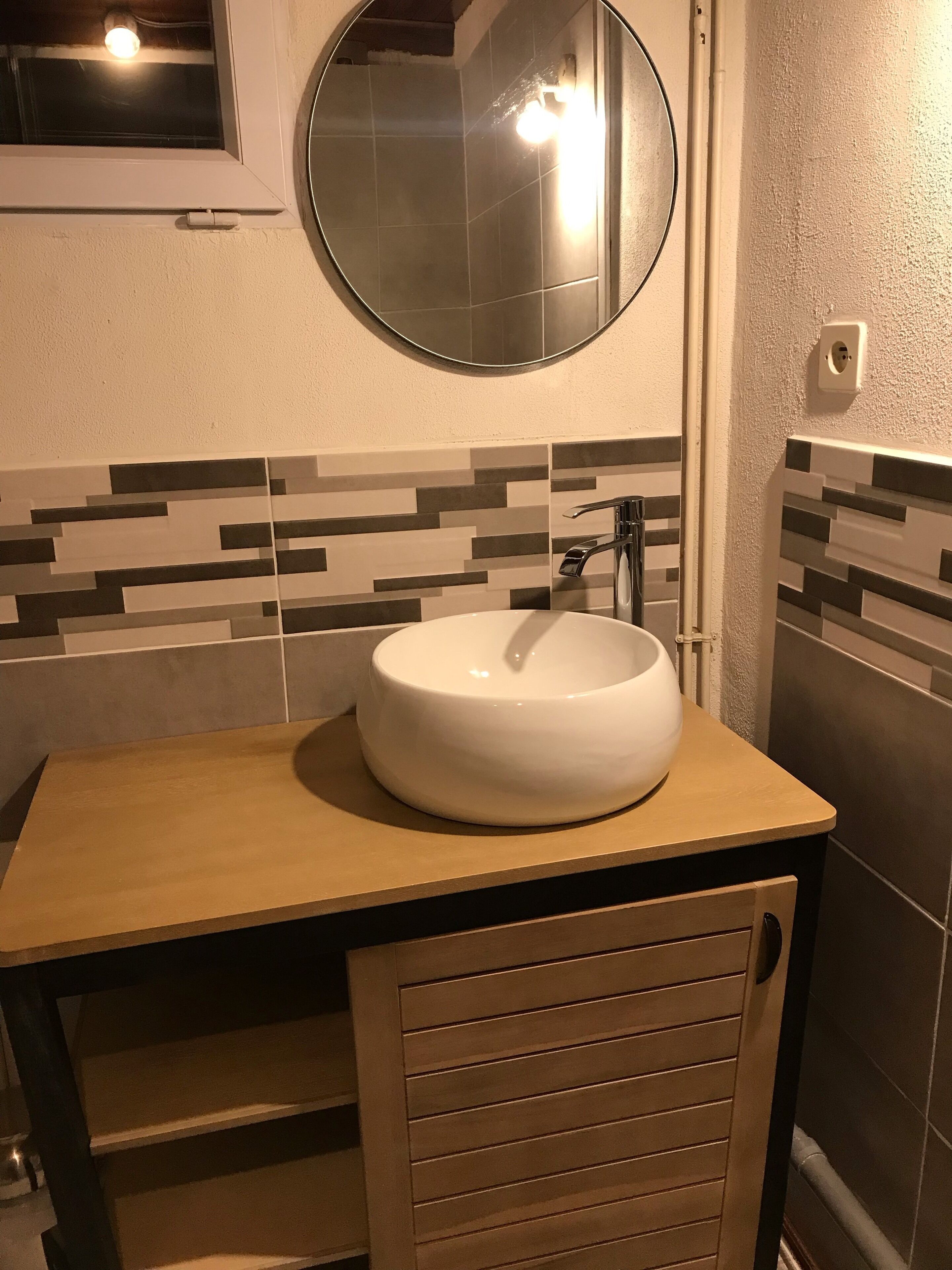 A bathroom with a round mirror, a white sink, and a wooden vanity.