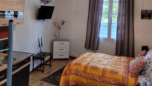 A bedroom with a bed, a desk, a chair, a TV on the wall, and a window with curtains. - Beautiful studio between Chateau and Loire (Saumur)